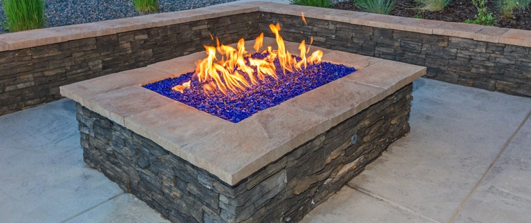 A wood burning fire pit built out of stone surrounded by chairs in our client's backyard in Nazareth, PA.